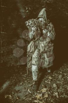 Post apocalyptic survivor, mysterious underground creature, stalker in gas mask and rags with runes, armed with handmade gun, hiding in dungeon, abandoned tunnel or city dark catacombs, sepia toned