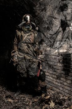 Survived in nuclear disaster or global ecological catastrophe human wearing rags, gas mask or air breathing apparatus and hiding in dark dungeon, catacombs or underground tunnel with handmade machete