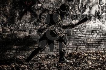 Post apocalyptic world survivor in gas mask, armed with handmade machete, running from darkness to light along dirty brick wall with graffiti. Stalker escaping from dangerous dungeon or city catacomb