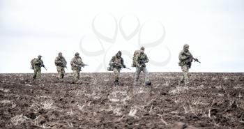 Army soldiers on march. Elite forces fighters group, commando tactical unit, reconnaissance team members in camouflage uniform, walking in line, carrying backpacks on muddy terrain