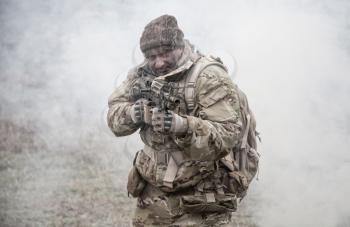 Soldier in camouflage uniform, wearing military ammunition, aiming service rifles, covering each other, shooting in competitors, attacking enemies trough smoke screen