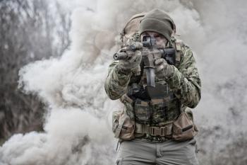 Soldier in camouflage uniform, wearing military ammunition, aiming service rifles, covering each other, shooting in competitors, attacking enemies trough smoke screen