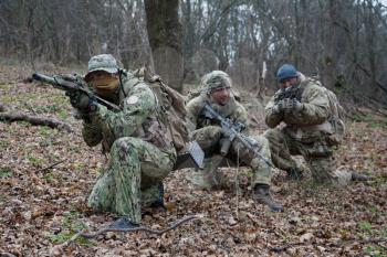 Army military soldiers team wearing camouflage uniforms and ammunition, armed assault rifles, machine gun replicas, hidings in woods, making ambush in forest, training in tactical teamwork
