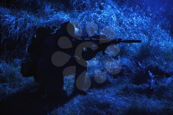 Army elite soldier, special forces fighter, infantry rifleman aiming service rifle with silencer in darkness, searching targets to shoot on stealth mission, spying and observing enemies positions