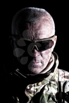 Army veteran, elderly commando fighter, experienced mercenary in camouflage uniform, wearing tactical glasses, looking in camera, studio, low key shoulder portrait on black background