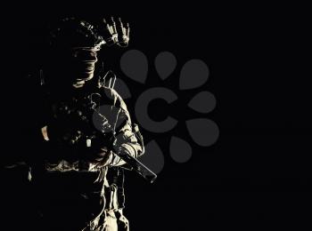 Army special operations forces soldier in mask and combat uniform, helmet equipped night-vision device, armed submachine gun with silencer, looking aside, low key studio portrait on black, copyspace