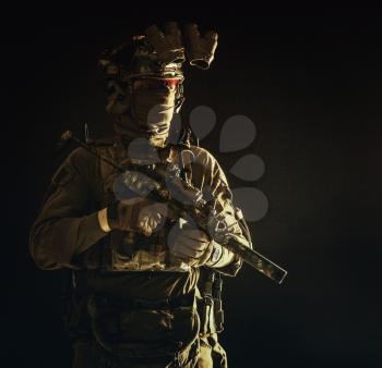 Half length, low key portrait of elite commando fighter, professional mercenary hiding identity behind mask, glasses, standing in darkness with mini submachine gun in hands, wearing nigh-vision device