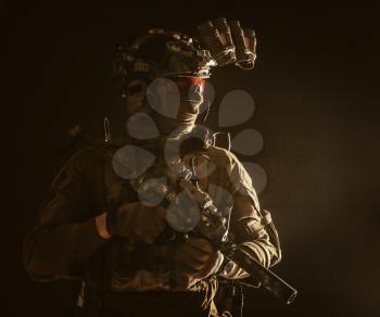 Army special forces tactical group fighter moving in darkness, using radio headset, looking through four lens night-vision, thermal imaging device on helmet, armed small submachine gun with silencer
