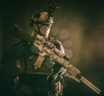 Army special operations soldier, counter-terrorist crew sniper, marksman in combat helmet, hiding face behind mask, armored service rifle with optical sight, low key studio shoot on blue background