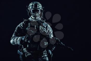 Army special operations forces soldier in mask and combat uniform, armed submachine gun, low key studio portrait on black, copyspace contour shot