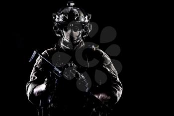 Army elite soldier with hidden behind mask and glasses face, in full tactical ammunition, equipped night vision device, radio headset, armed short barrel service rifle studio contour shot