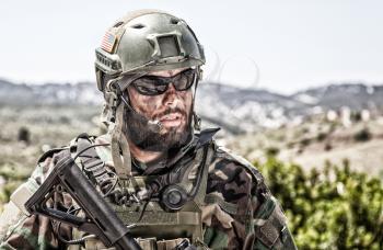 Shoulder portrait of army soldier, special forces fighter, modern warfare combatant with dirty, unshaven face, wearing sunglasses, combat helmet and talking in tactical radio headset during mission