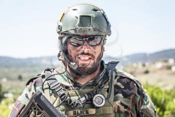 Shoulder portrait of army soldier, special forces fighter, modern warfare combatant with dirty, unshaven face, wearing sunglasses, combat helmet and talking in tactical radio headset during mission