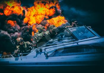 Navy SEALs team fighters rushing on speed boat, breaking through enemy fire during military mission. Army special operations forces soldiers sailing on boat, exposure with black smoke on background