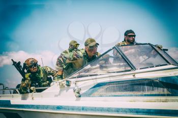 Navy SEALs team fighters, army special operations soldiers squad, in combat uniform, armed submachine gun and service rifle, going fast on speed boat, chasing and attacking enemy, patrolling seacoast