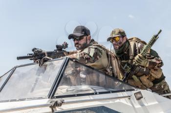 Navy SEALs team fighters, army special operations soldiers squad, in combat uniform, armed submachine gun and service rifle, going fast on speed boat, chasing and attacking enemy, patrolling seacoast