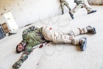 Dead soldier lying on floor after been shoot in stomach. Wounded army infantryman in bloodied uniform, lying on ground without consciousness. SEALs team fighter killed during action, fallen in battle