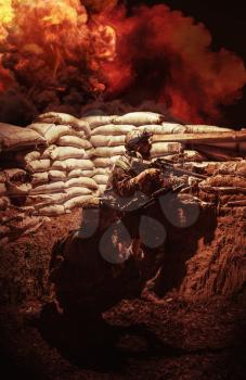 Special operations soldiers, SEALs team fighters armed with service rifle taking cover from enemy fire behind sandbags in trench. Soldiers at battlefield, fiery explosions, smoke clouds in background