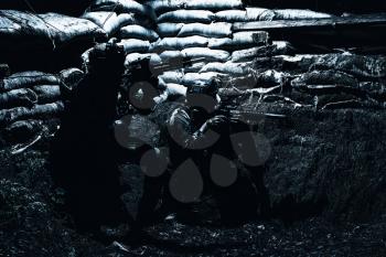 Soldiers covering from enemy fire in trench. Two Navy SEALs fighters, infantrymen in camouflage uniform and helmet, armed service rifles, hiding behind sandbags during night attack or gunfight