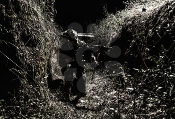 Army soldier, special forces infantryman in combat uniform and helmet, armed assault rifle, sneaking in darkness, crawling in trench at night. Commando fighter, combatant hiding from enemy fire