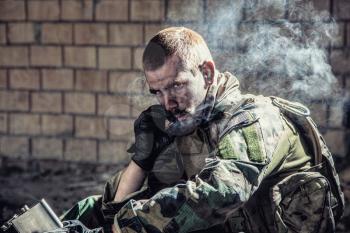 Special forces soldier after the fight sitting in ruined building smoking cigarette staring at the camera