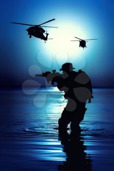 Army soldier with rifle night moon silhouette under cover of darkness in action during raid crossing river in the water. Combat helicopters are supporting operation from air