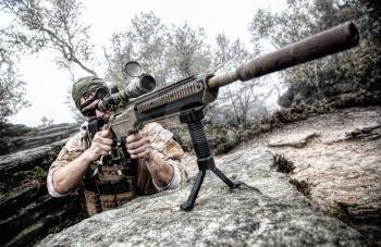 Private military contractor PMC sniper in baseball cap with assault rifle in the rocks