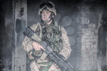 Special forces soldier, Marine Corps infantryman, commando fighter in helmet and body armor, equipped tactical radio, armed with service rifle with optical sight and grenade launcher in smoky ruins
