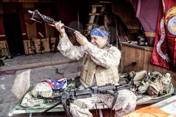 Marine Corps machine gunner with confederate flag bandana on head, disassembling, making maintenance of service weapon, checking gun barrel after cleaning at improvised outpost in abandoned building