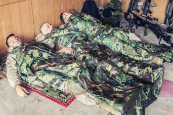 Tired U.S. marines resting at temporary base or camp, lying on floor in uniform and tactical ammunition, covered with poncho liners and sleeping bags, sleeping well after hard raid, exhausting mission