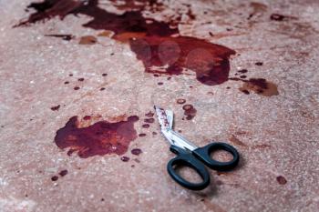 Trauma shears or bandage scissors lying on floor with stains of human blood around. Blood loss and bleeding stop, emergency medical aid for gunshot wounds, tactical combat casualty care on battlefield