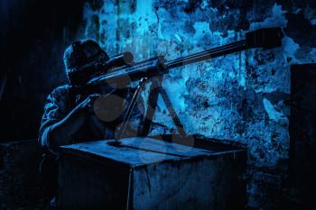 Army sniper night ambush in ruined building. Marine rifleman aiming with optical opscore and shooting in darkness with large caliber, anti-materiel sniper rifle. Secret military mission, urban warfare