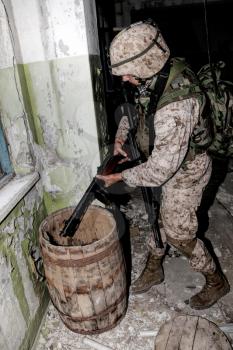 U.S. marine, special forces soldier holding in hands and examining automatic weapons of World War II, found in wooden barrel at old, abandoned building during anti terrorist raid or clearing mission