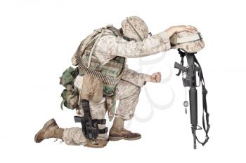 Army soldier in sorrow for fallen comrade, standing on knee, leaning on rifle with helmet and two dog tags on chain, studio shoot isolated on white. Military funeral honors, grief for killed in action