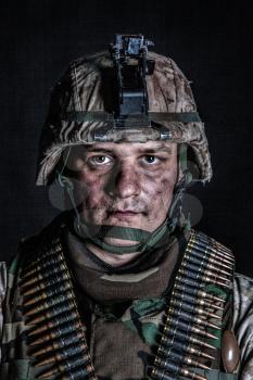 Shoulder portrait of experienced army soldier, military conflict veteran, skilled marine fighter in ragged camouflage uniform, advanced helmet and ammo belts on chest, studio shot on black background