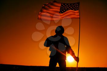 Silhouette of US army soldier, special operations shooter holding waving on flagpole national flag while standing on background of sunset. American army hero, United States or America military victory