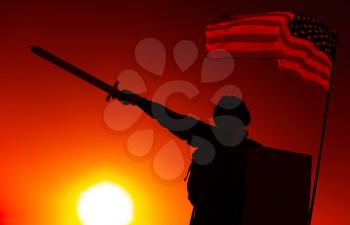 Silhouette of USA army soldier standing under national flag, holding shield, raising and pointing sword forward on sunset background. Soldier duty and honor, national hero and military victory concept