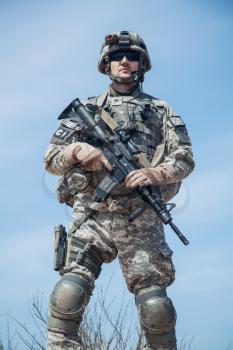 Portrait of United states airborne infantry man with arms, camo uniforms dress. Combat helmet on, tactical light, radio and knee pads protection