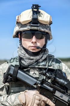 Portrait of United states airborne infantry corporal with arms, camo uniforms dress. Combat helmet on, tactical light, radio microphone on his mouth