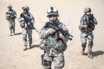 Team of United states airborne infantry men with arms, camo uniforms dress. Front view, some militants of squad are defocused and blurred