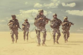 Team of United states airborne infantry men with weapons moving patrolling desert storm. Sand, blue sky on background of squad, sunlight, front view
