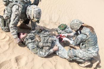 Battlefield medic saving life of injured airborne infantry paratrooper on desert sand. Wounded warrior screaming pain suffering but he will be alive