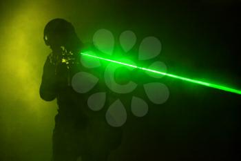 Studio shot of swat police operator with laser sights on rifle. Fire smoke screen green background. Laser rays beams diagonal