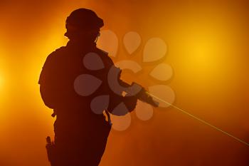 Studio shot of swat police operator with laser sights on rifle. Fire smoke screen orange background. Laser rays beams