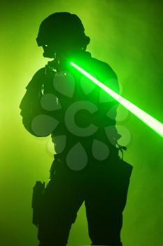 Studio shot of swat police operator with laser sights on rifle. Fire smoke screen green background. Laser rays beams diagonal