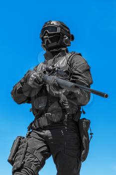 Swat police operator with sniper rifle in black uniforms. Low angle view, blue sky background