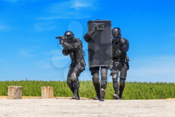 Swat police special forces operators storming criminals terrorists hiding behind ballistic shield. Blue sky daylight
