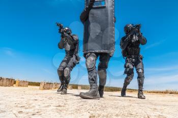Swat police special forces operators storming criminals terrorists hiding behind ballistic shield. Blue sky daylight, low angle front view