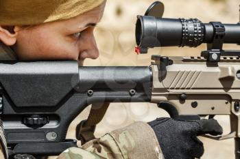 Young female sniper in camouflage with gun in the desert