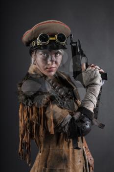 Nuclear post apocalypse life after doomsday concept. Grimy female survivor with homemade weapons. Studio portrait on black background
